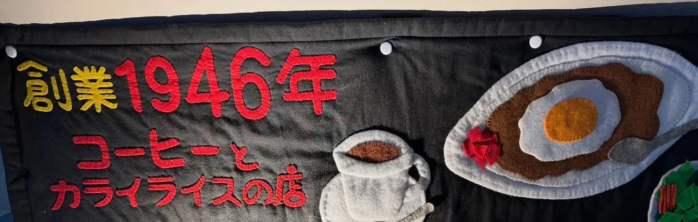 黒い布に創業1946年と「コーヒーとカライライスの店」を縫い付けた看板